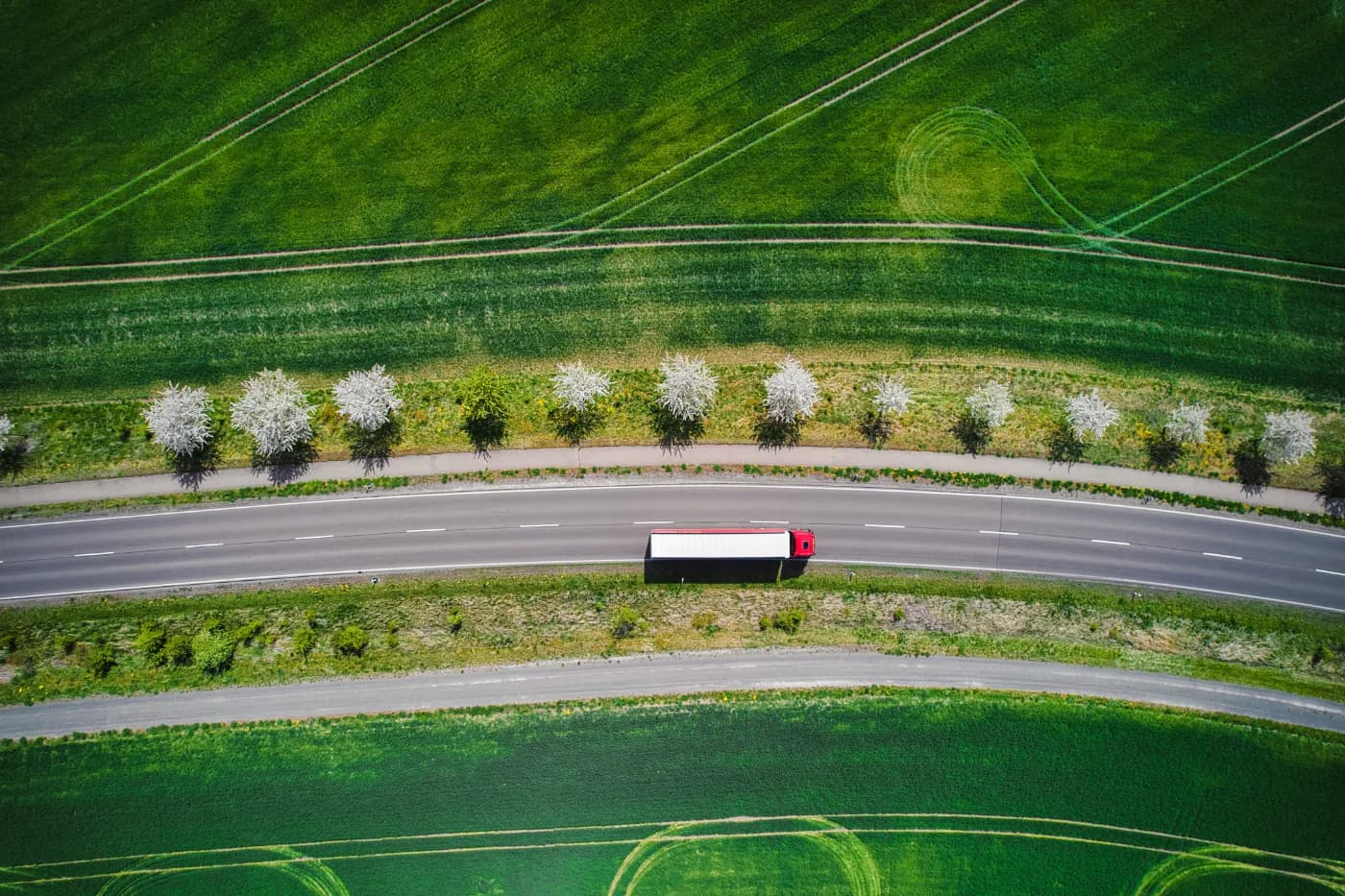 Aerial view of an articulated lorry on a road curving between green fields.