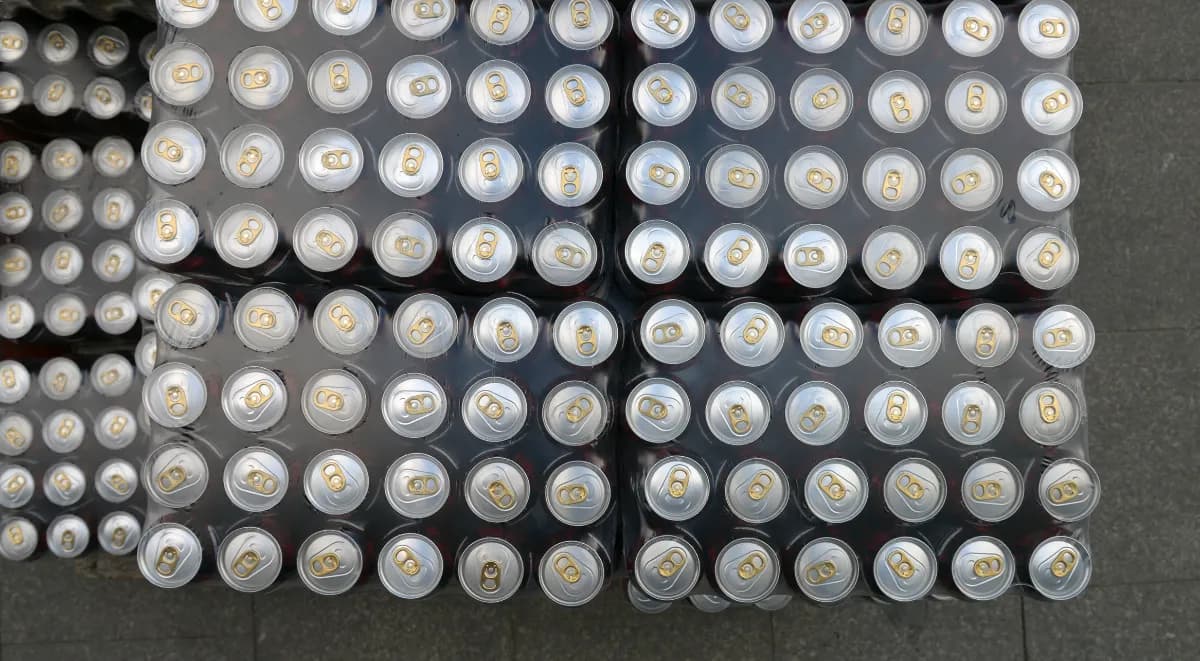 Shrink-wrapped trays of canned drinks stacked on pallets, seen from above.