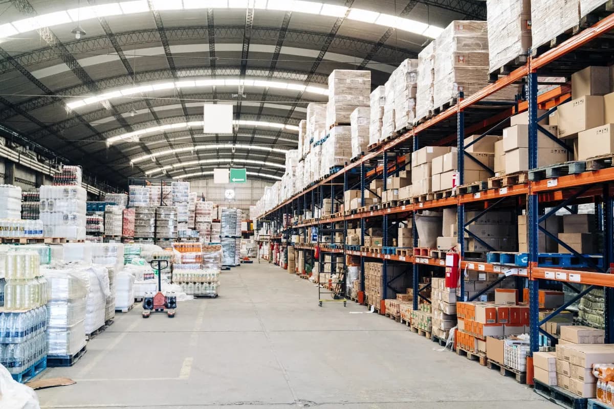 Warehouse aisle between pallets of bottled drinks and racking loaded with mixed cartons.
