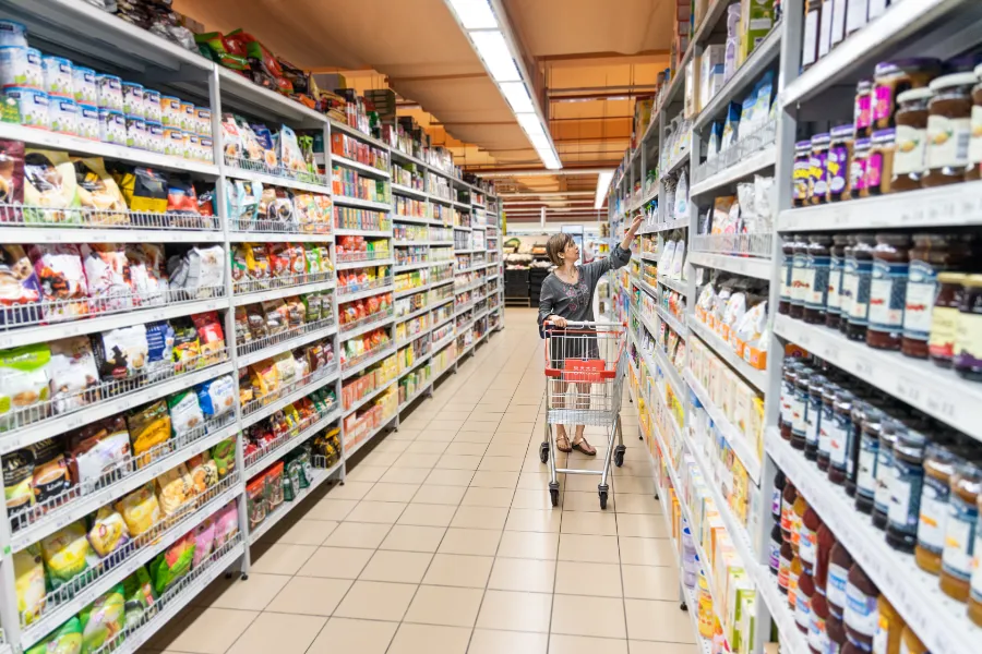 Image a lady with a trolley in a supermarket aisle of FMCG goods, such as foods, drinks and more.