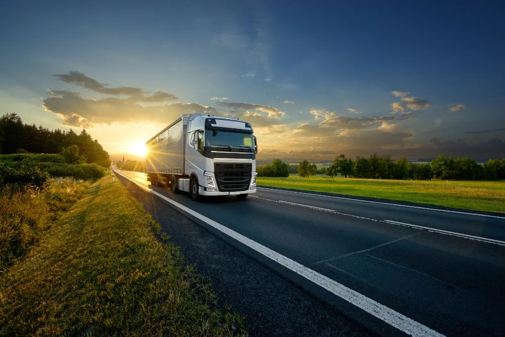 Truck travelling down the road with the sunset behind it. The truck is loaded ready with surplus stock ready to be used elsewhere.
